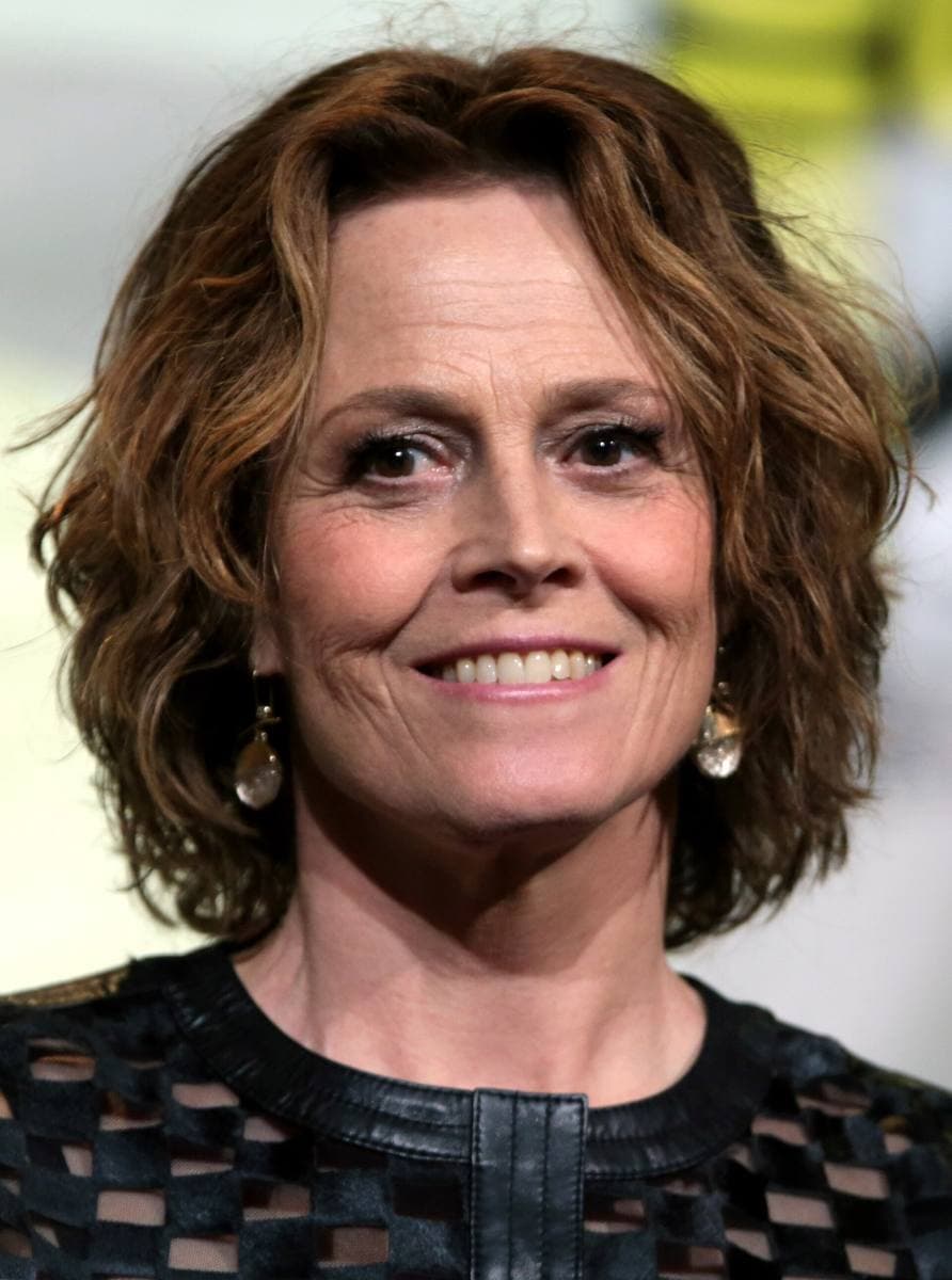 Sigourney Weaver smiling, short curled brown hair