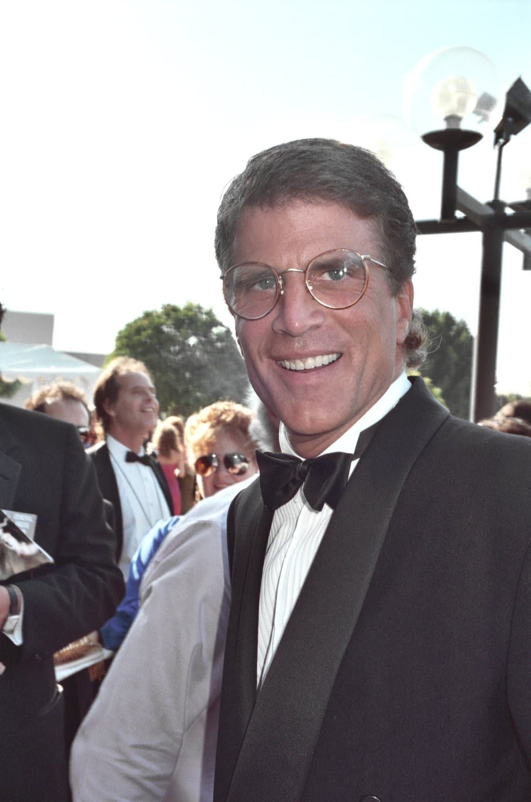 Ted Danson smiling in a tuxedo and round glasses on a red carpet