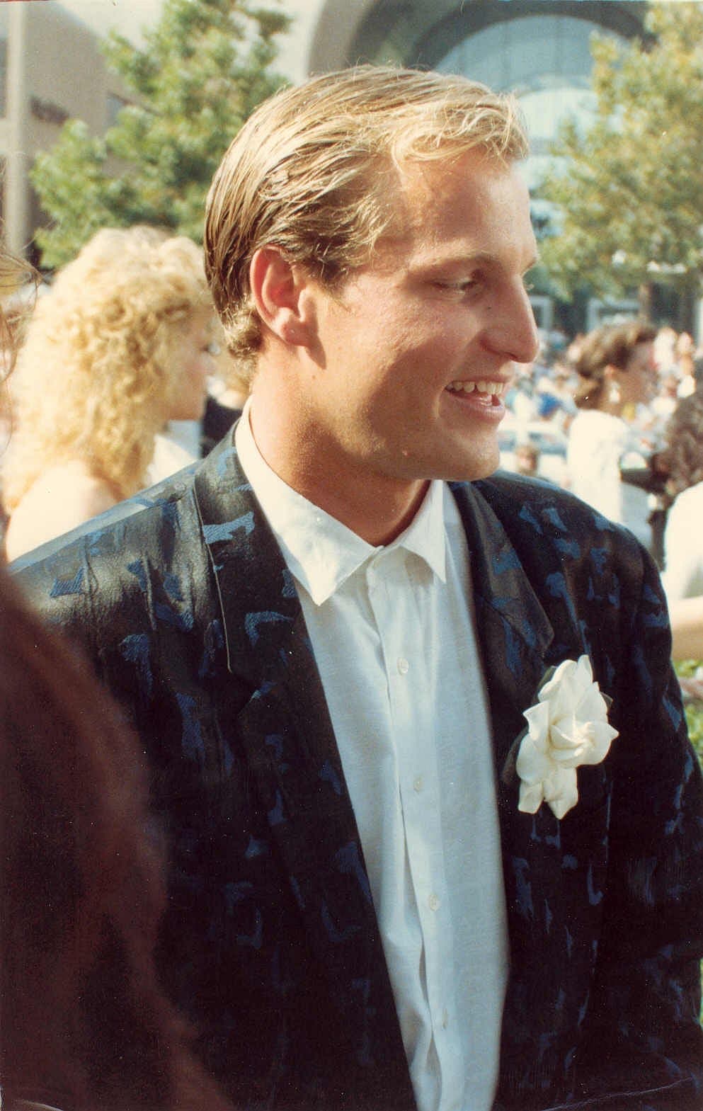 A young Woody Harrelson in a patterned jacket with a white flower in the lapel