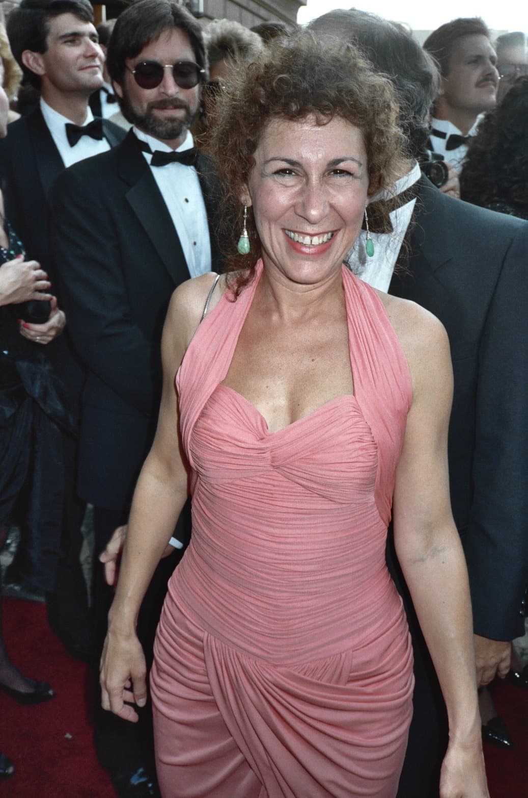 Rhea Perlman laughing in a pink draped dress on a red carpet