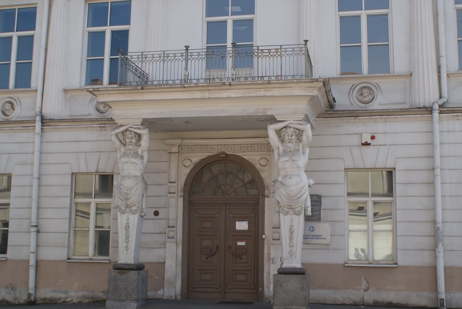 A white palace front with an arched door between two stone atlantes