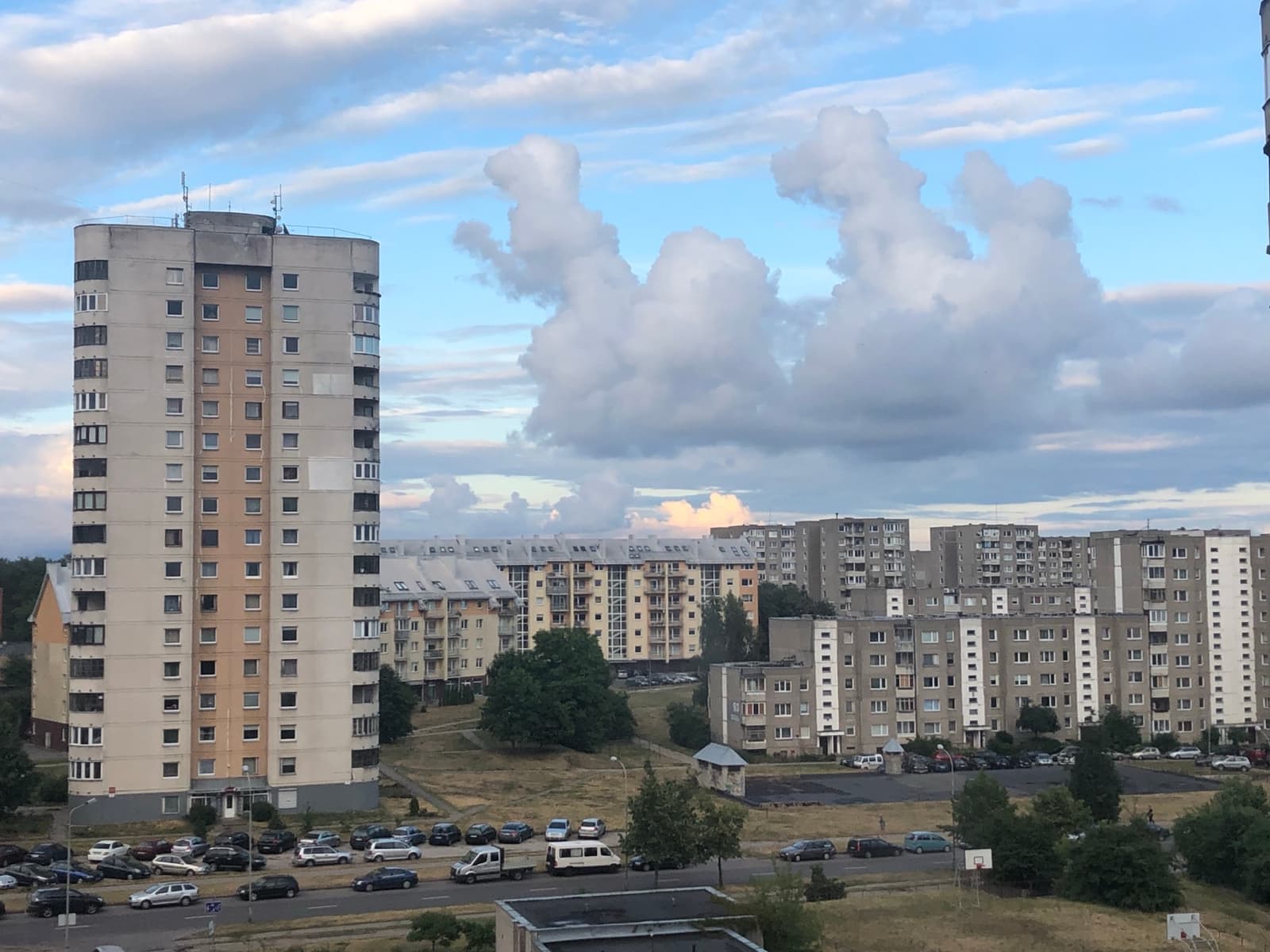 A tall concrete apartment tower and lower blocks behind a car park