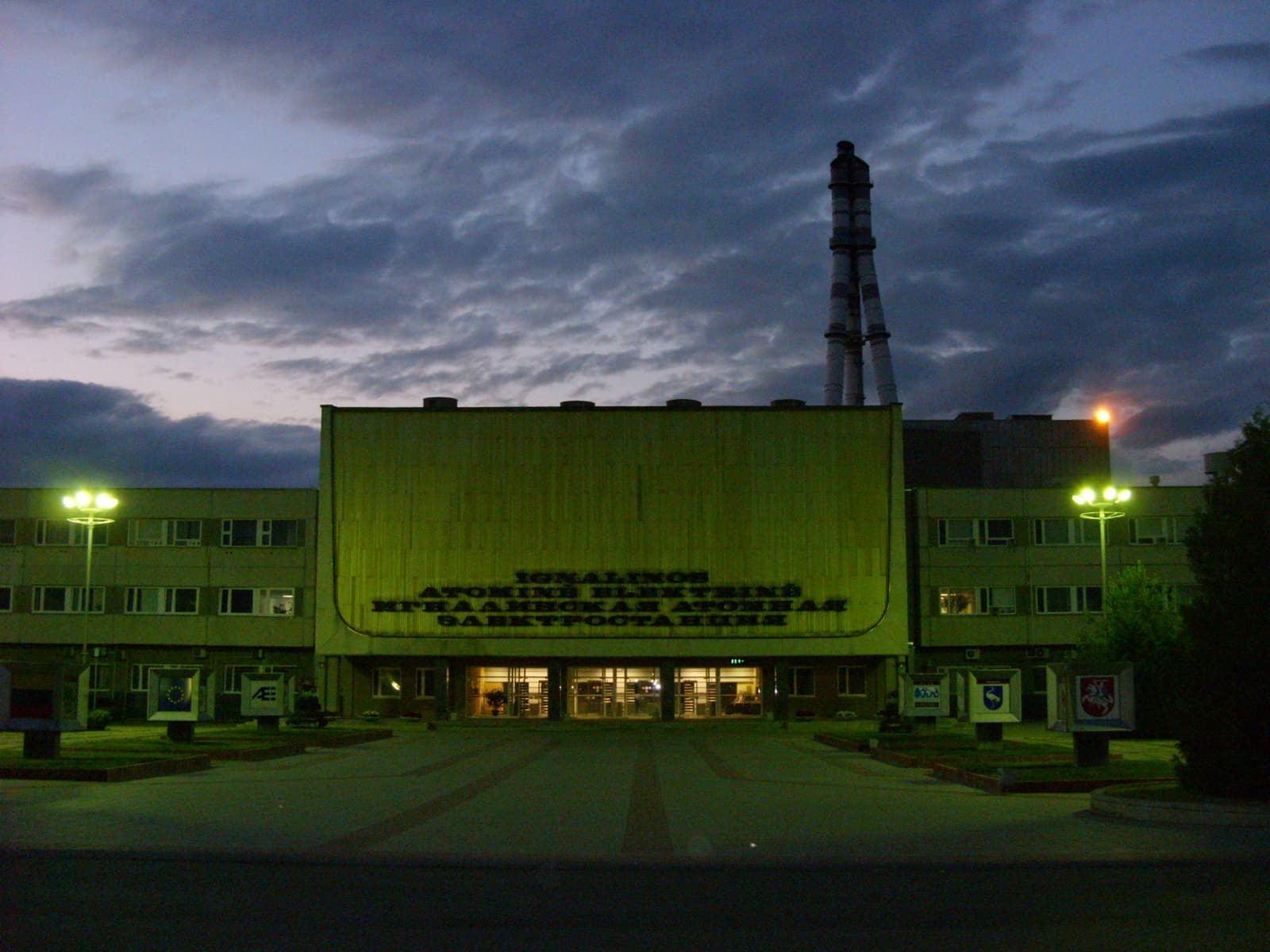 The front of the Ignalina plant lit green at dusk, a stack behind
