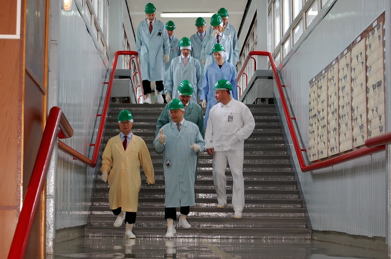 A group in white coats and green helmets coming down a staircase