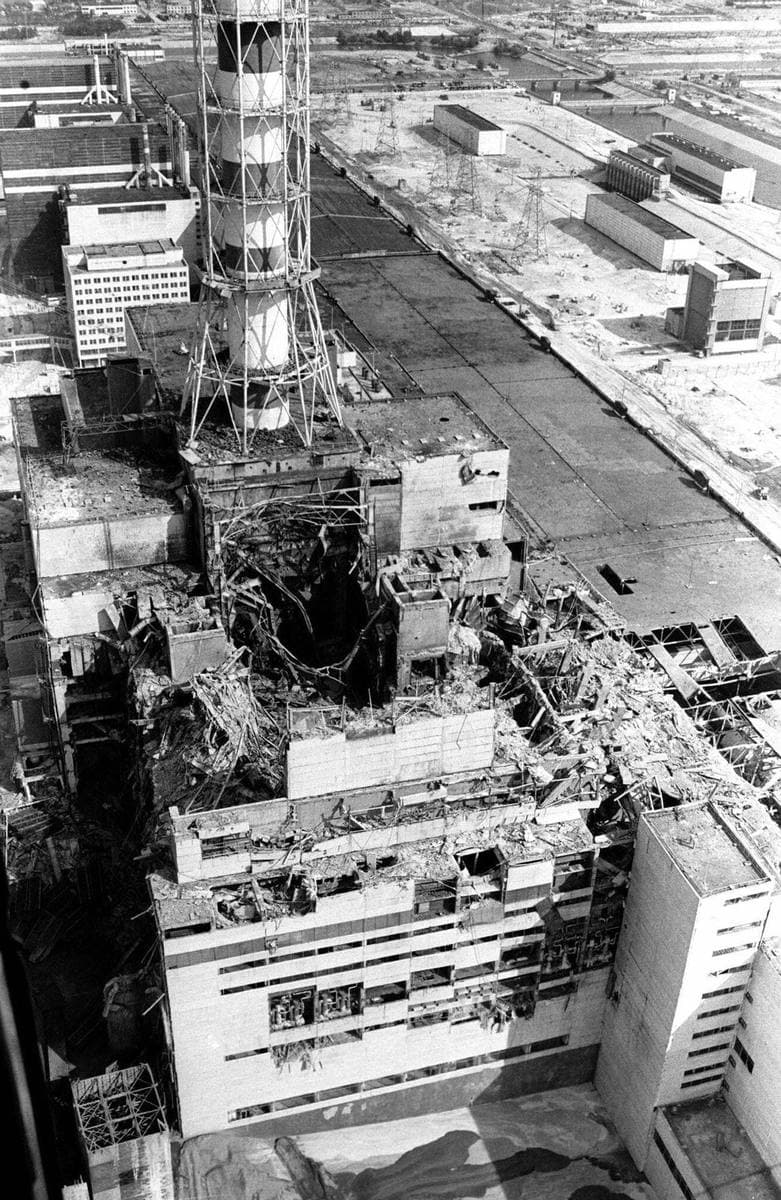 Aerial black-and-white view of the wrecked reactor building beside its ventilation stack
