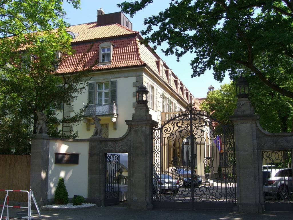 A cream palace front behind tall wrought-iron gates and stone gateposts