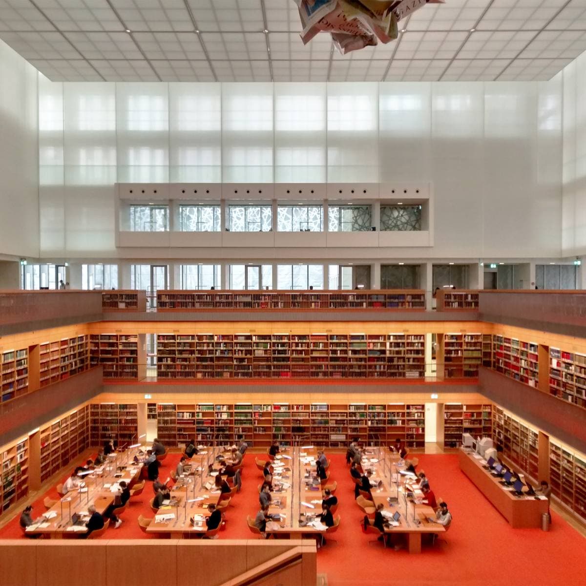 A tall white reading room with rows of desks on a red floor and galleries of shelves