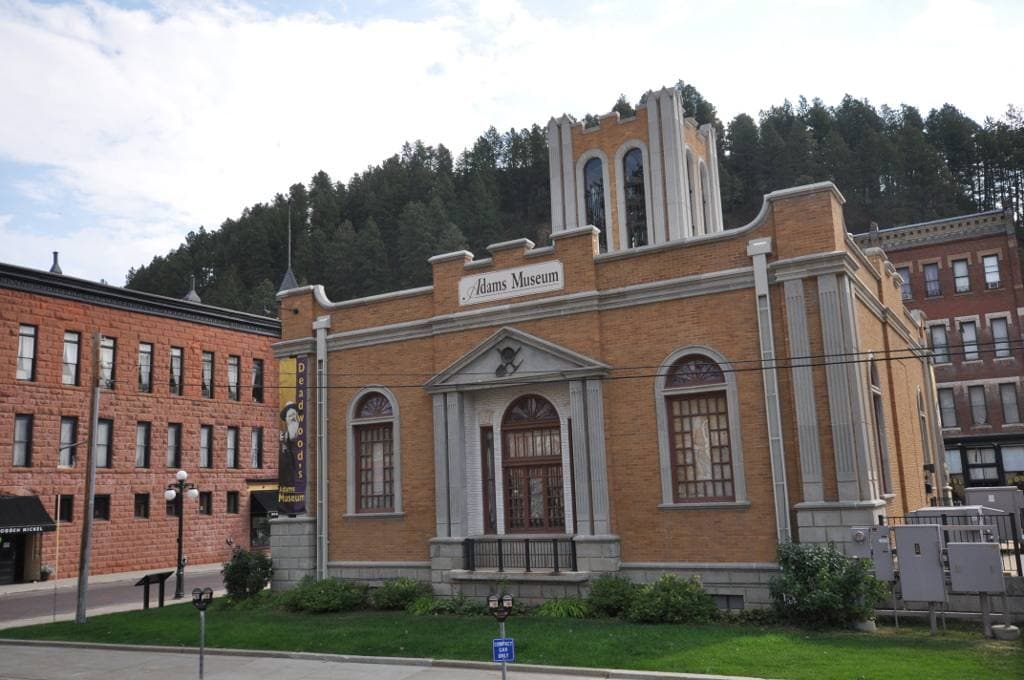 A pale brick museum building with arched windows and a lawn in front