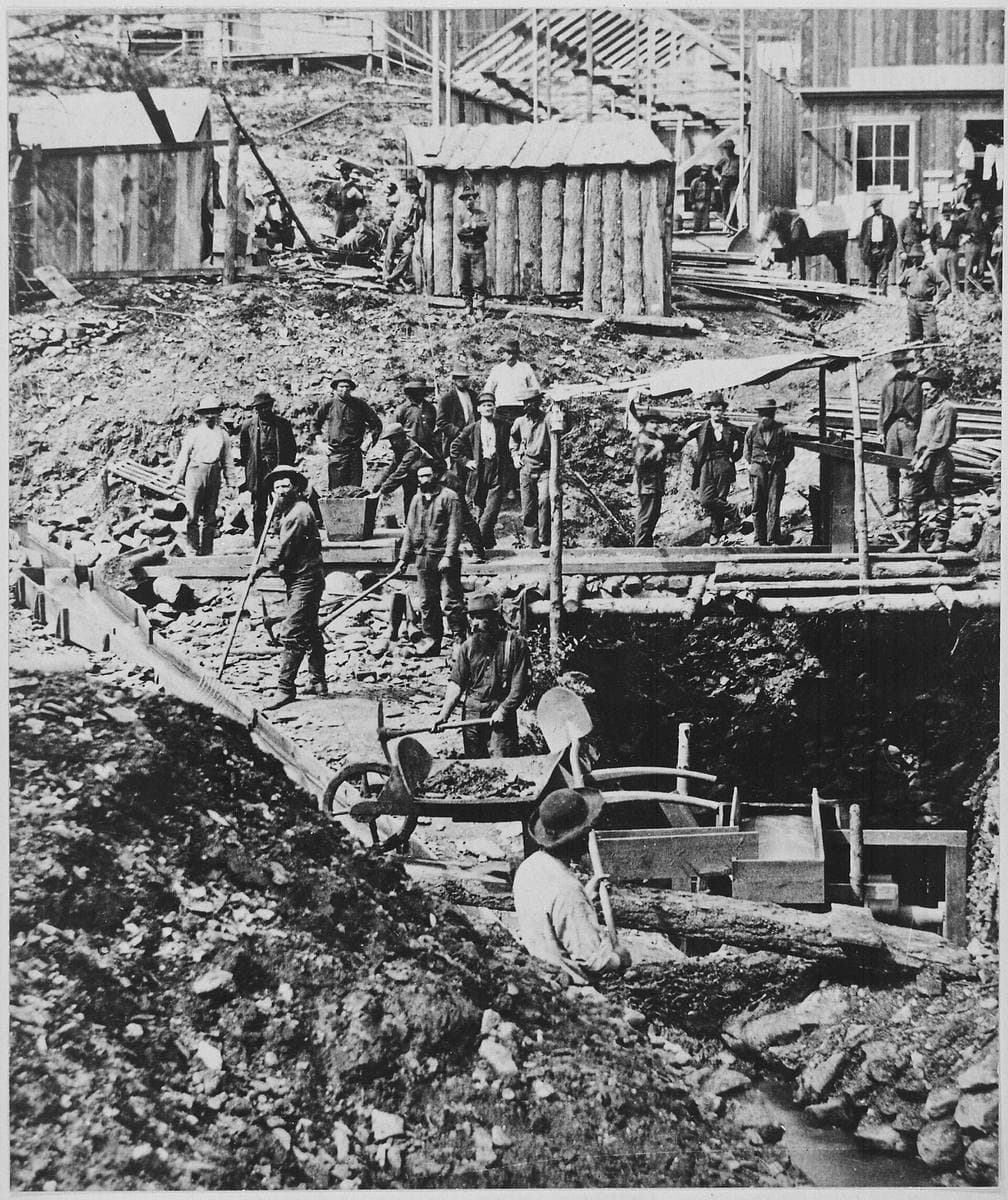 Men digging and sluicing in a gulch while bystanders watch