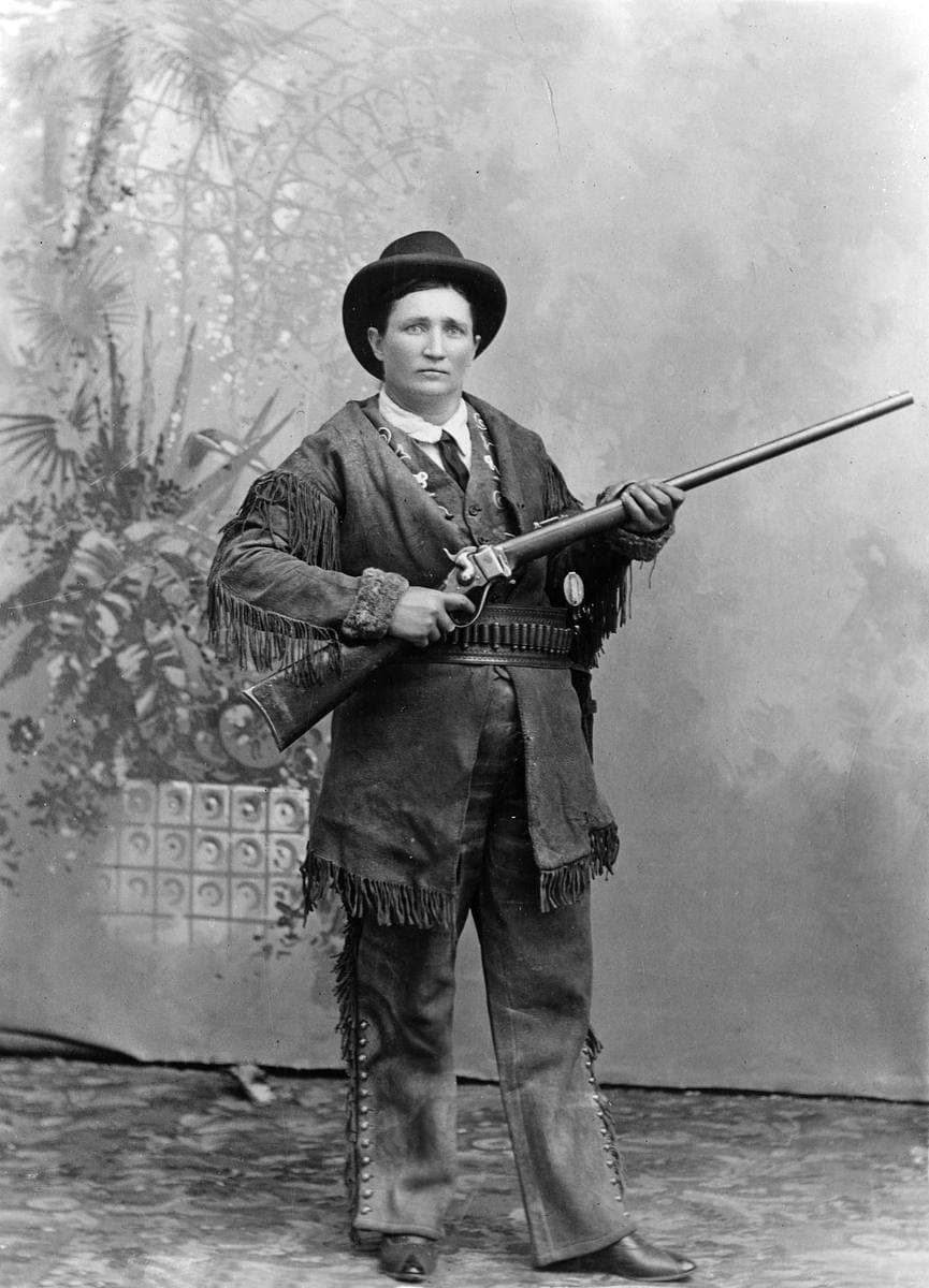 Calamity Jane standing in buckskins with a rifle in a studio