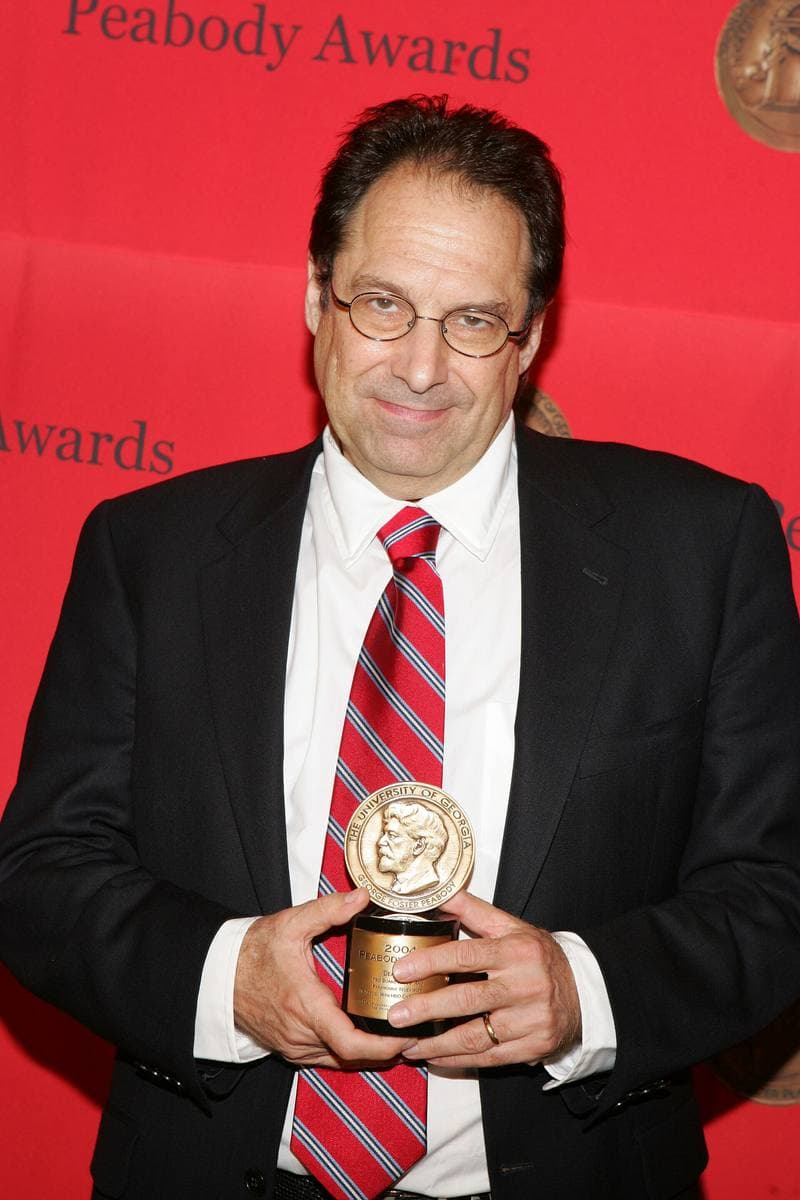 David Milch holding a Peabody medallion in front of a red wall