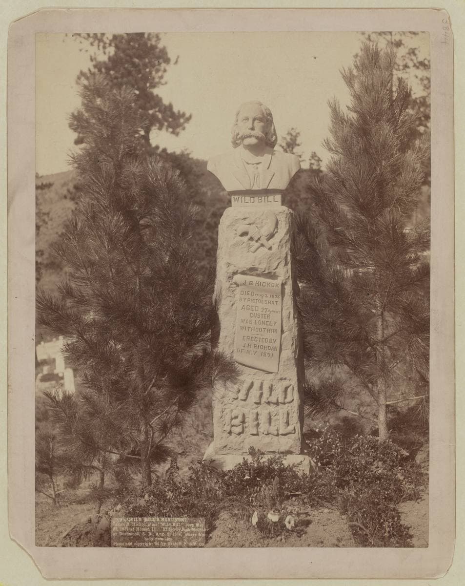 A carved stone monument with a bust on top, among pines