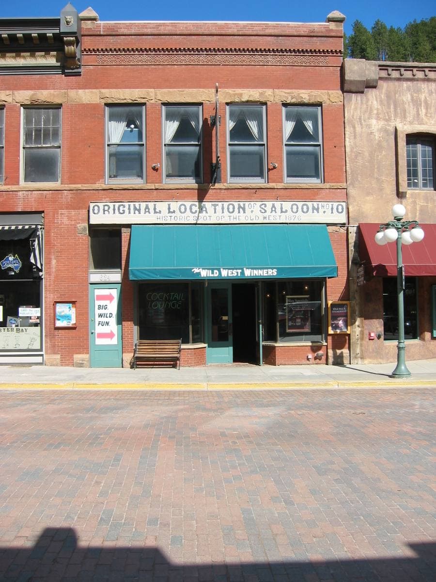 A red-brick storefront with a teal awning, signed Original location Saloon No. 10