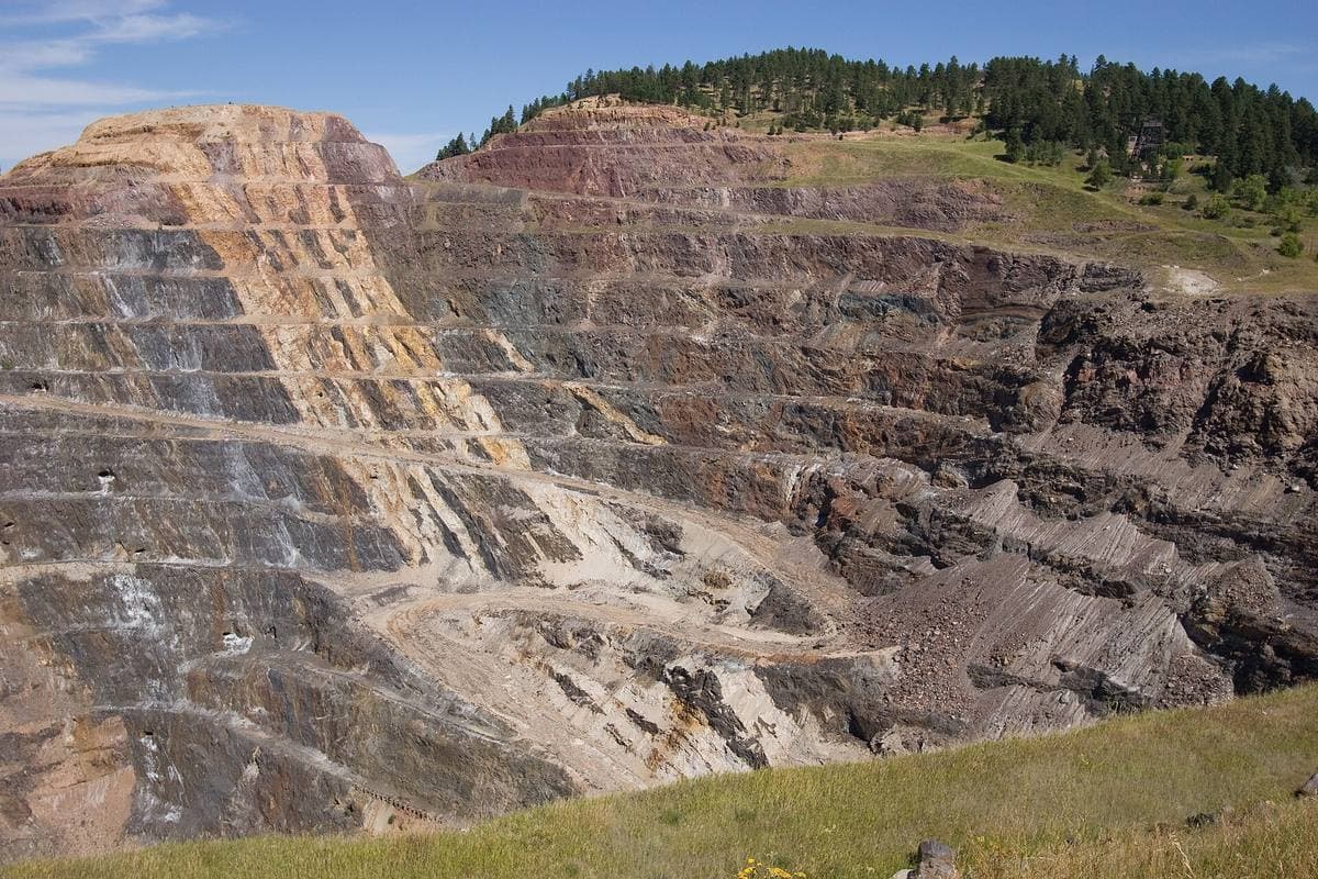 A huge stepped open pit cut into a hillside, banded in grey and ochre