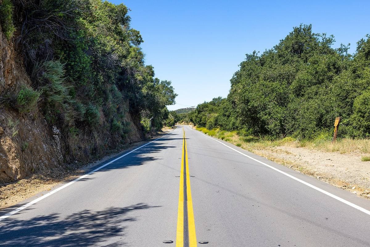 A two-lane road with a yellow centre line running between oak-covered hills
