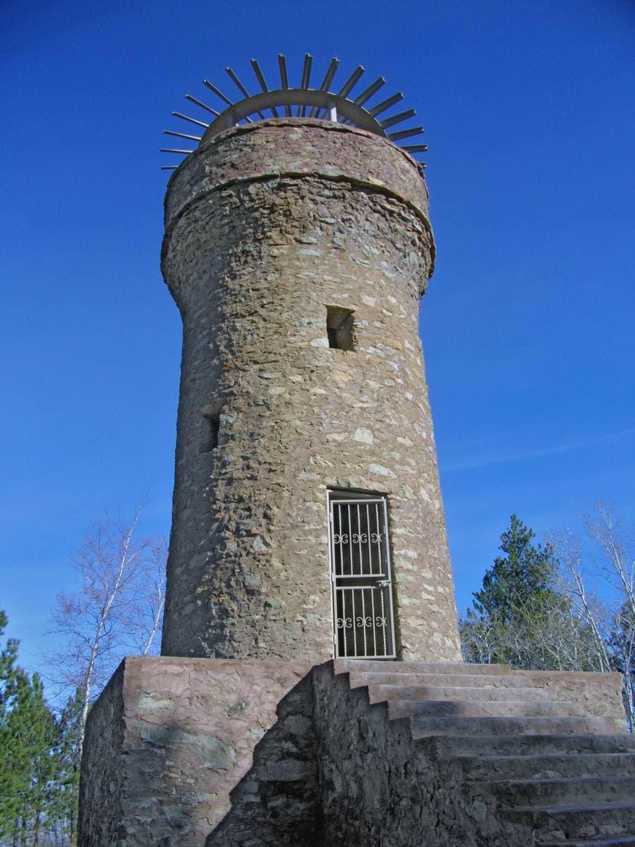 A round stone tower with a crown of iron spikes against a blue sky