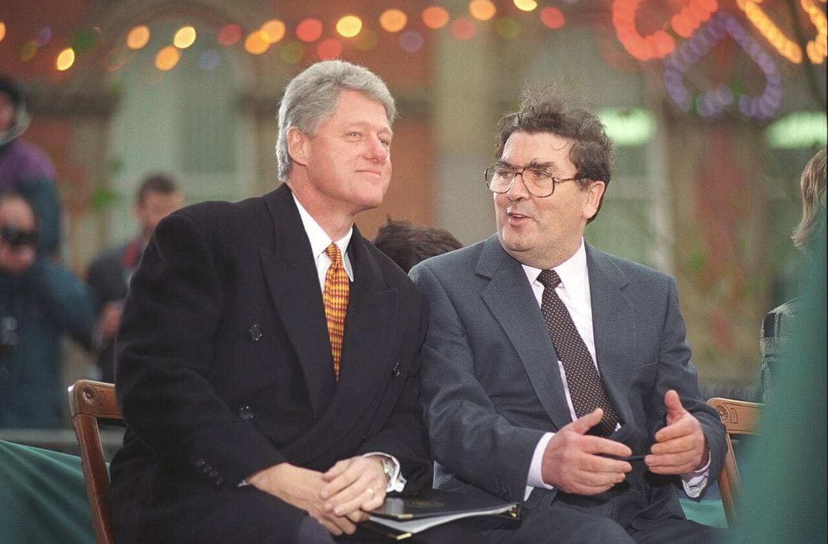 Bill Clinton and John Hume seated together, both smiling, in dark suits