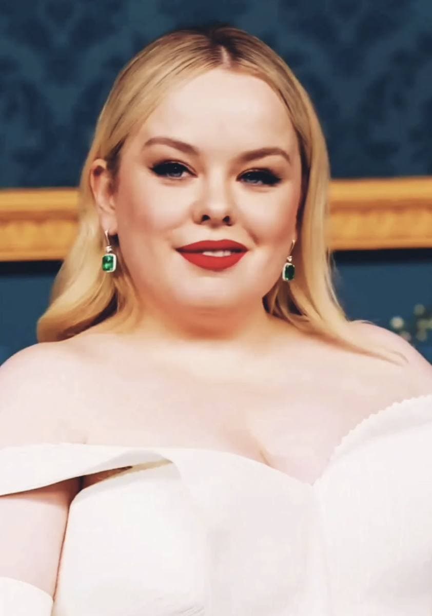 Nicola Coughlan, smiling, in a pale off-the-shoulder dress against a blue wall