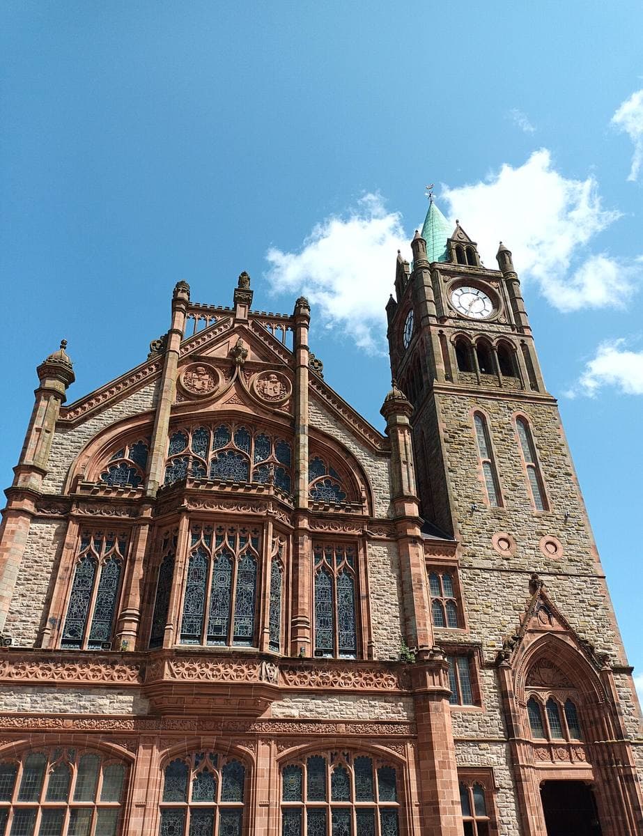 A red sandstone Gothic hall with a tall clock tower under a blue sky