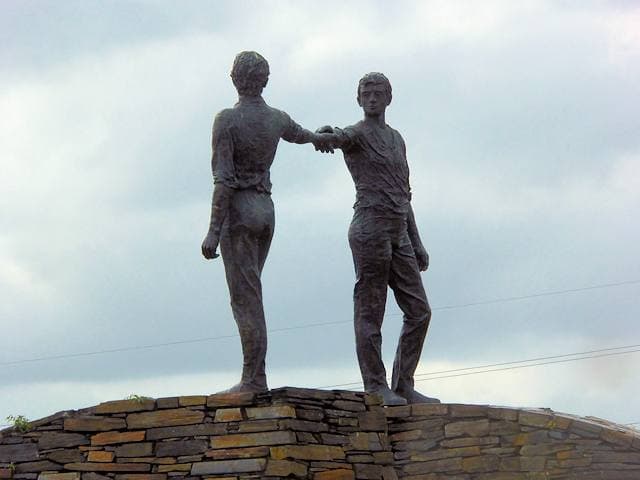 Two bronze figures on a stone base, reaching towards each other