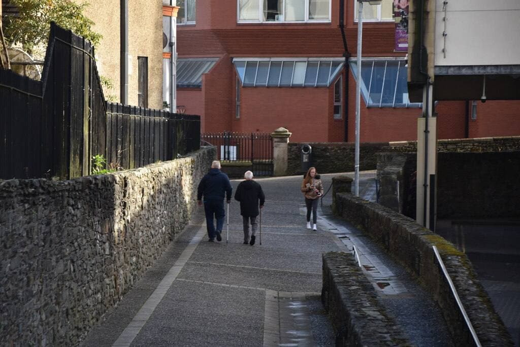 Two people walking along the paved top of the old city walls between stone parapets