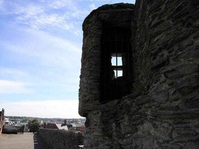 A round stone turret with a barred window on the city walls, rooftops beyond