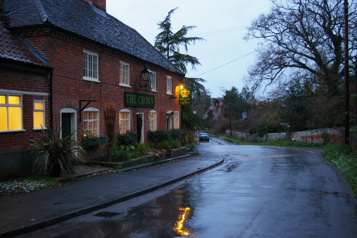 A brick pub with lit windows beside a wet village road under bare trees