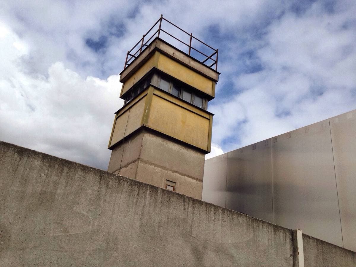 A concrete watchtower behind a grey wall under blue sky