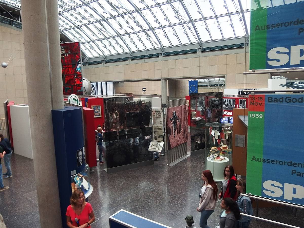A glass-roofed museum hall full of exhibits and visitors