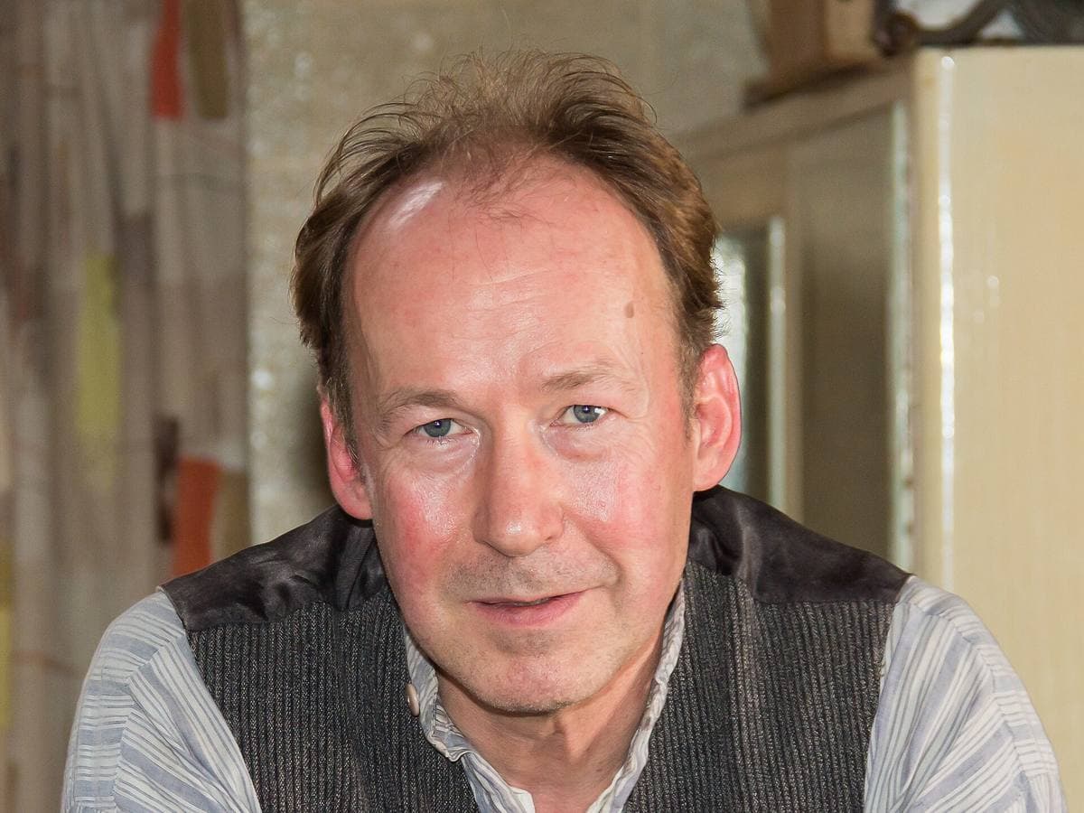 Ulrich Noethen in close-up, in a grey waistcoat, in a period kitchen set