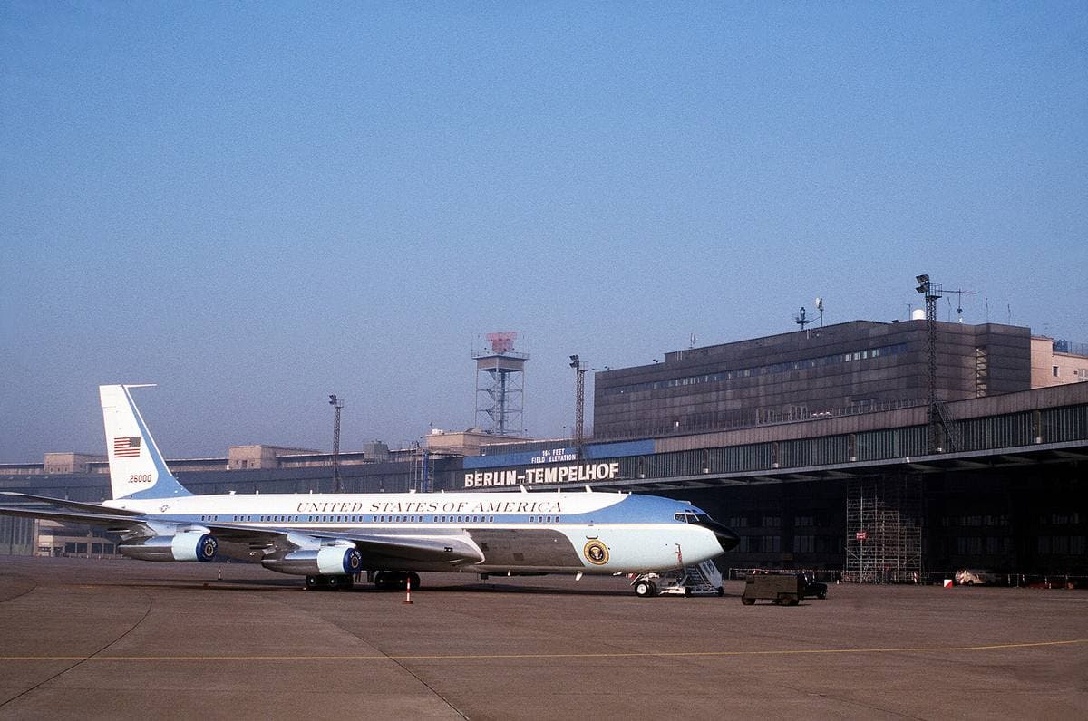 A white and blue Boeing jet parked under a long airport canopy