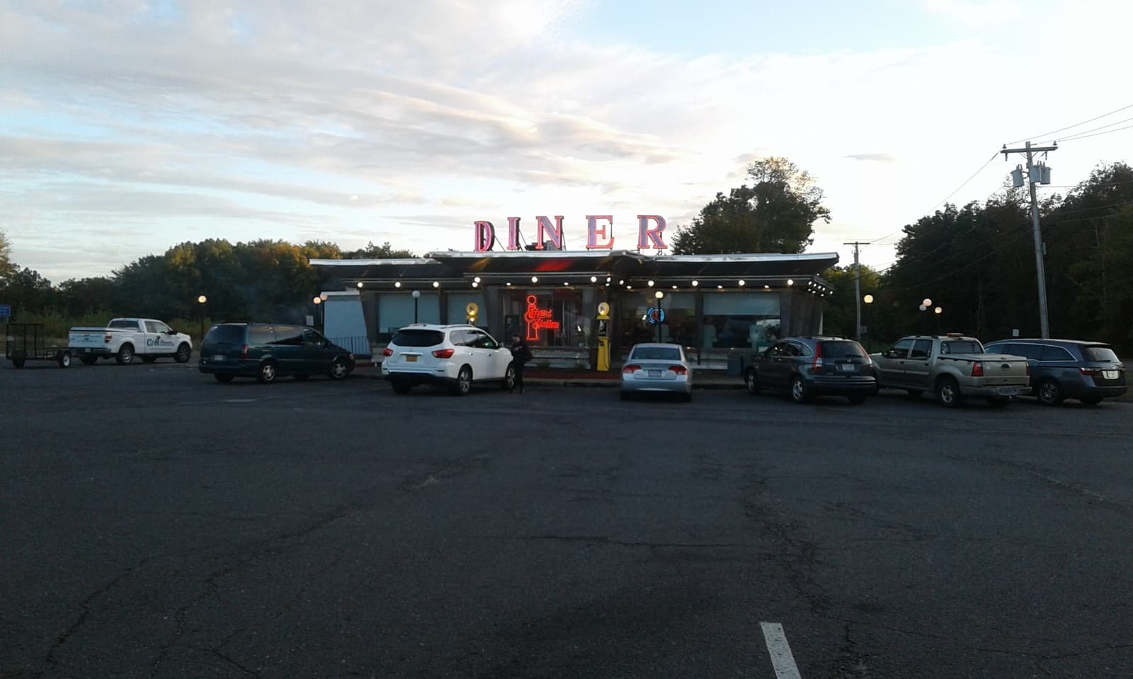 A roadside diner with a red neon sign at dusk