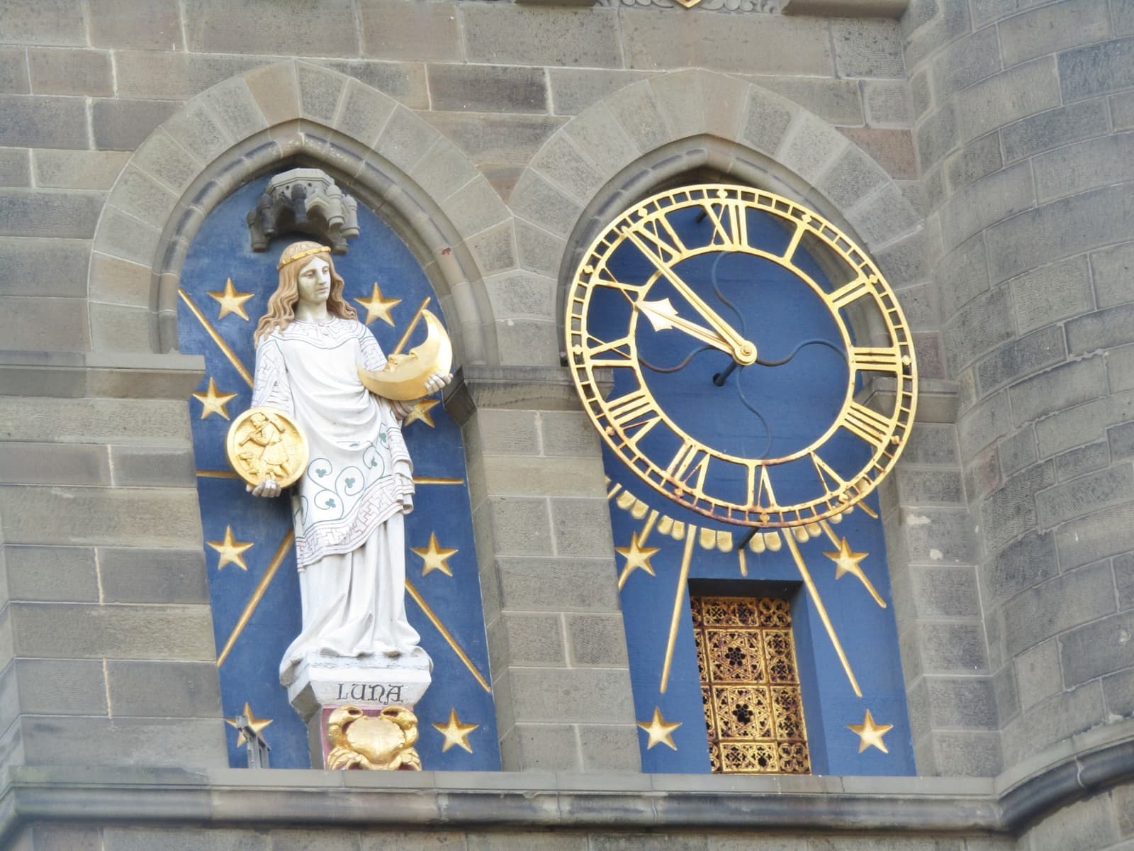A blue and gold clock face beside a painted figure on Cardiff Castle’s Clock Tower