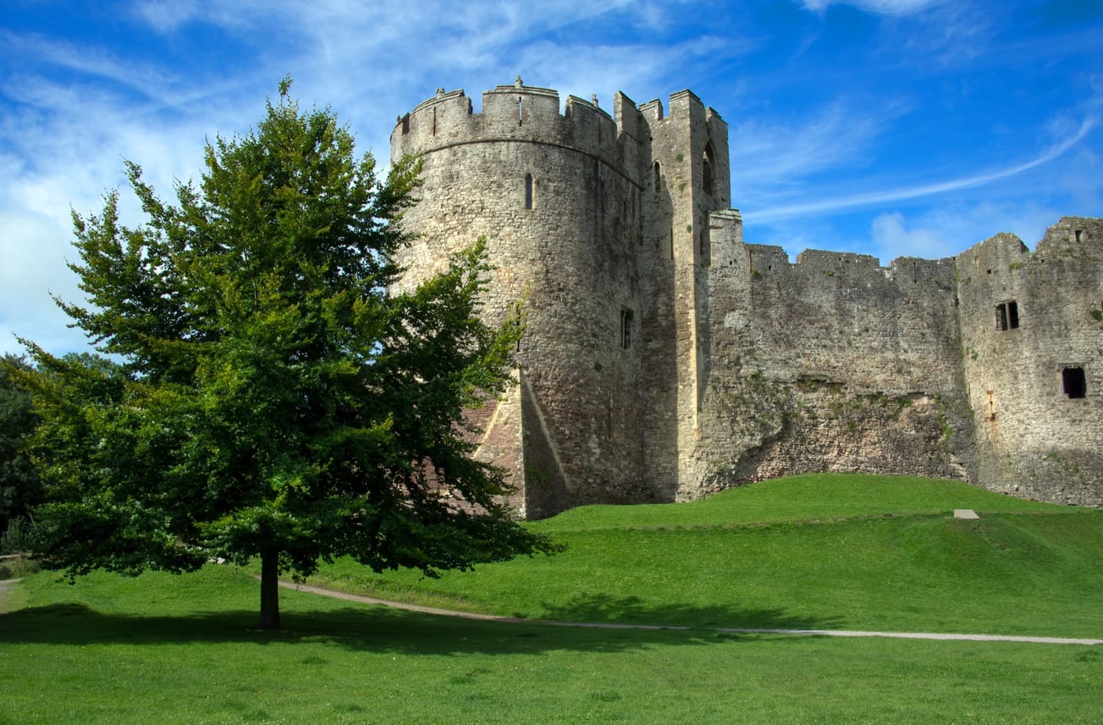 The round tower and curtain walls of Chepstow Castle above a lawn