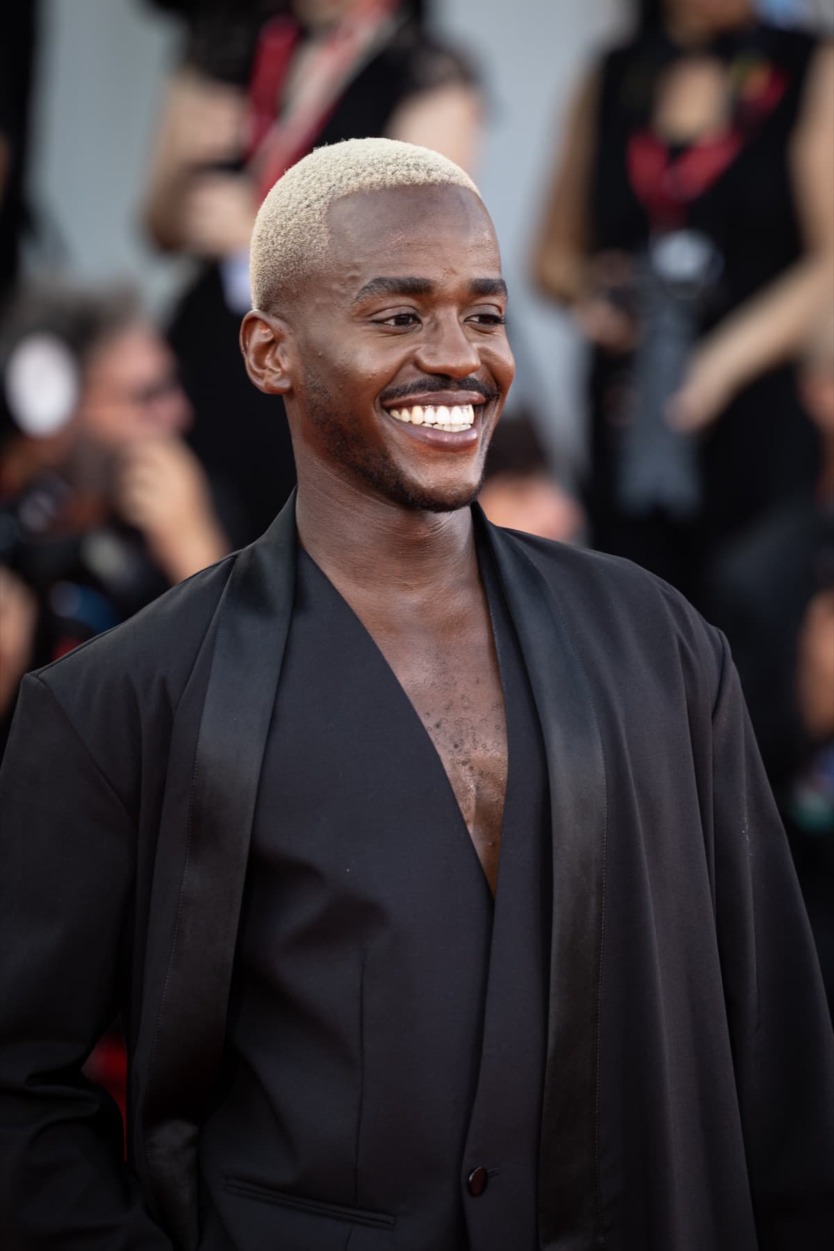 Ncuti Gatwa smiling on a red carpet in a black robe