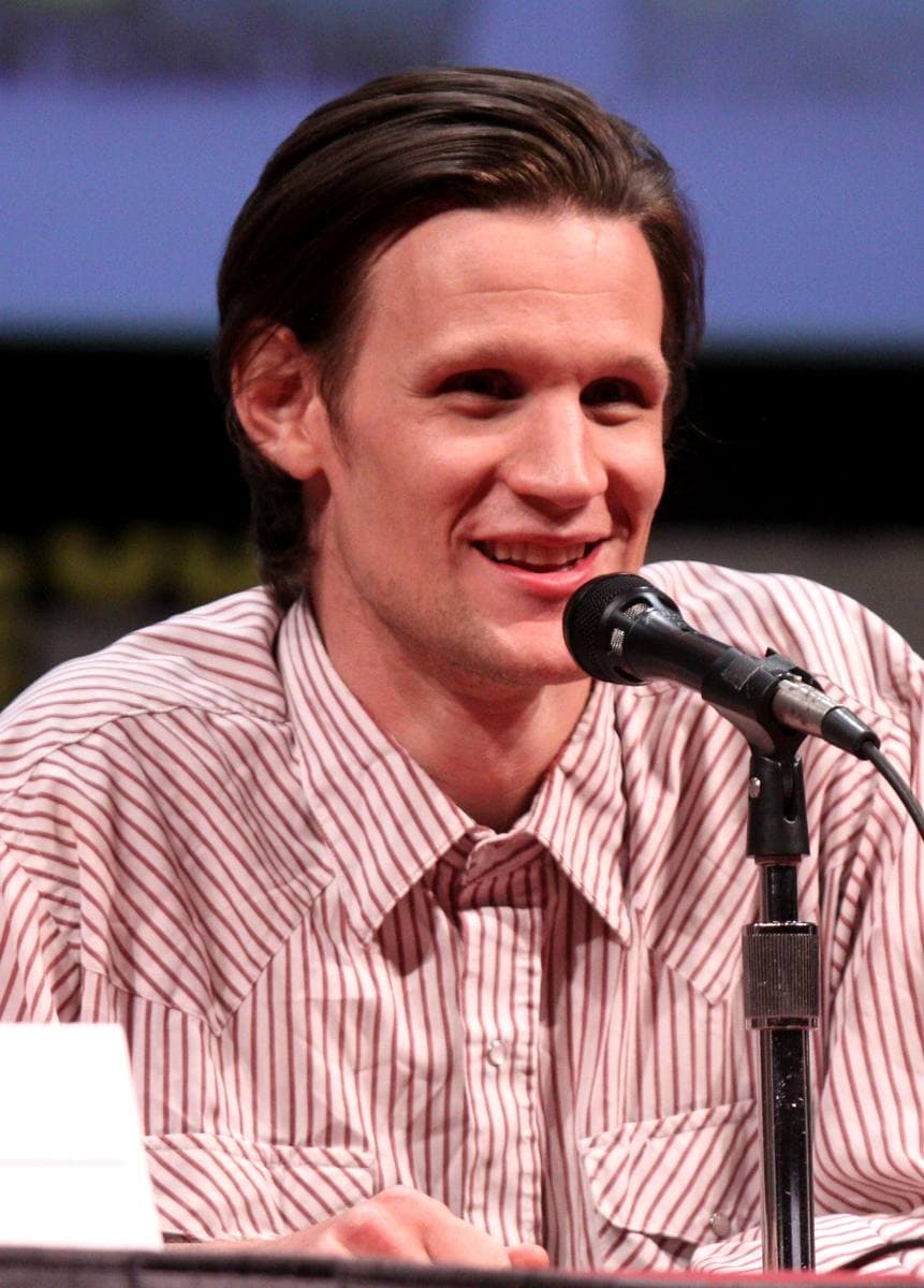Matt Smith, smiling, in a striped shirt at a panel microphone