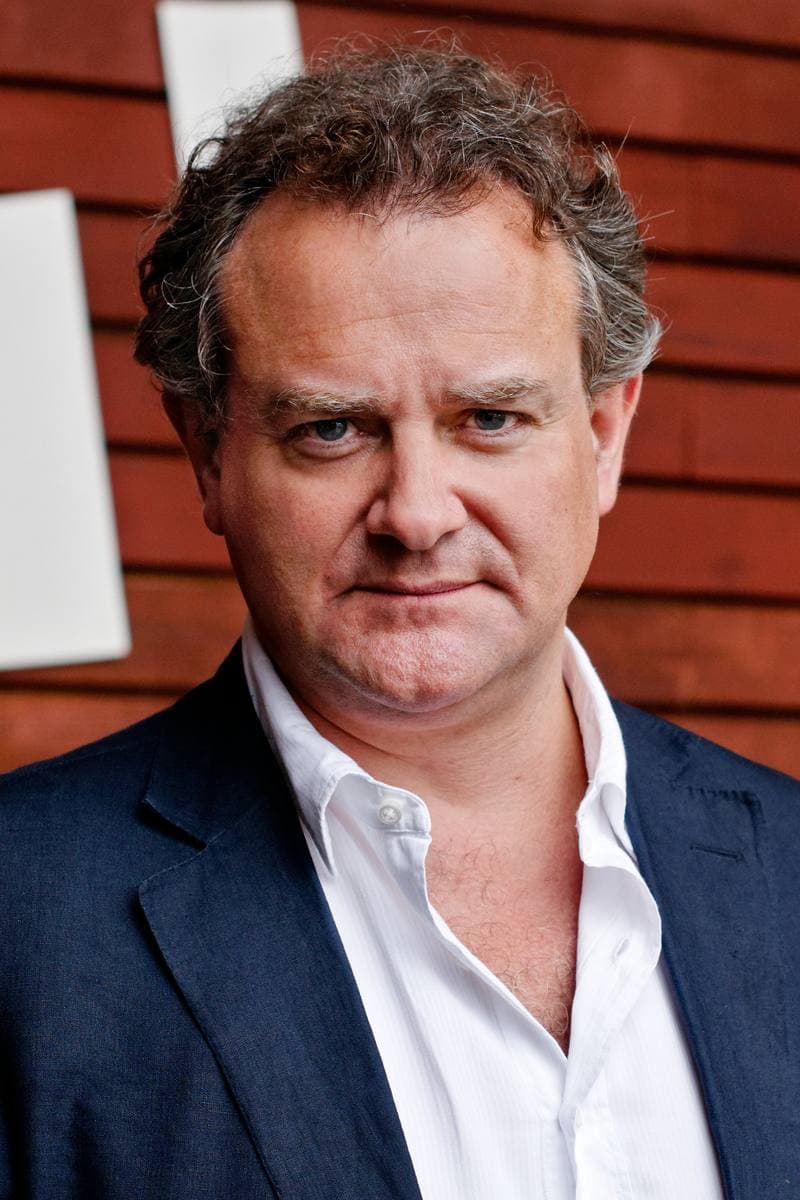 Hugh Bonneville in a dark jacket and open white shirt