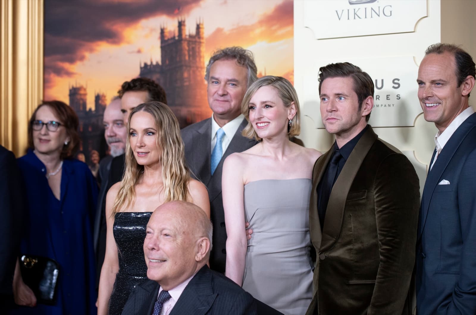 Julian Fellowes seated in front of Joanne Froggatt, Hugh Bonneville, Laura Carmichael, Allen Leech and Harry Hadden-Paton on a red carpet