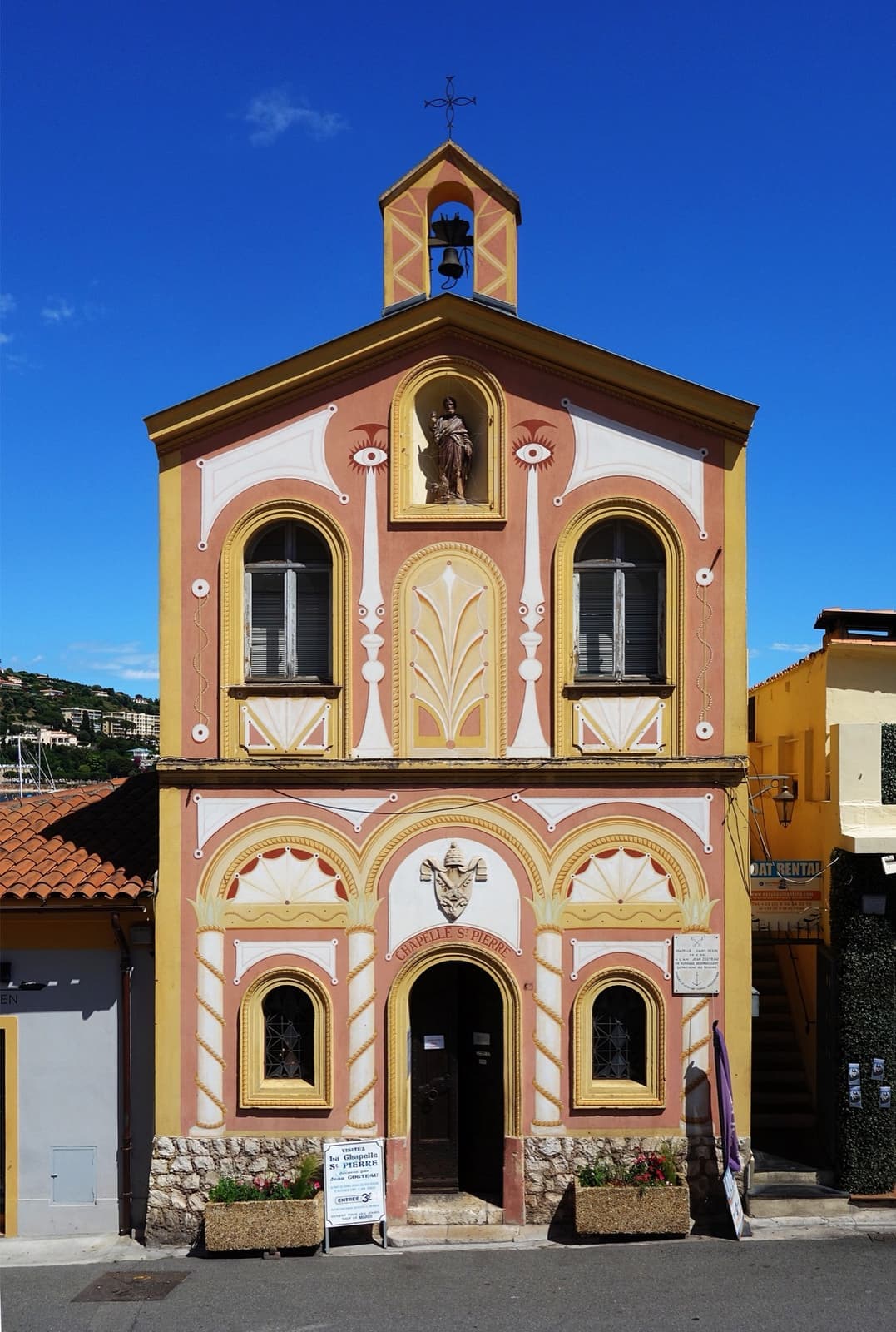 A small harbour chapel with a painted ochre and white facade and a little bell gable