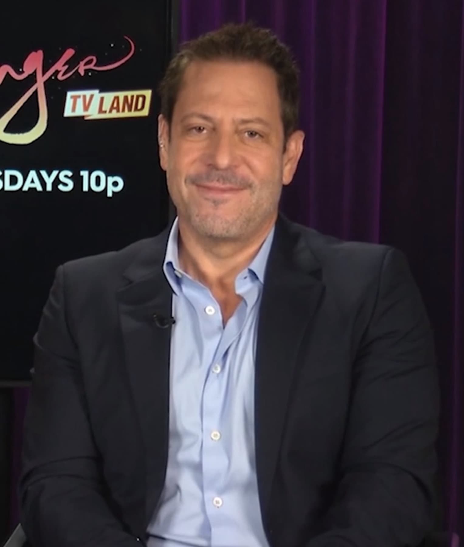 Darren Star in a dark jacket and open-necked blue shirt, smiling