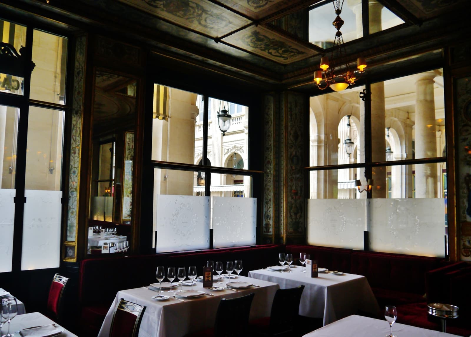 A restaurant room with painted glass panels, gilt frames and white tablecloths
