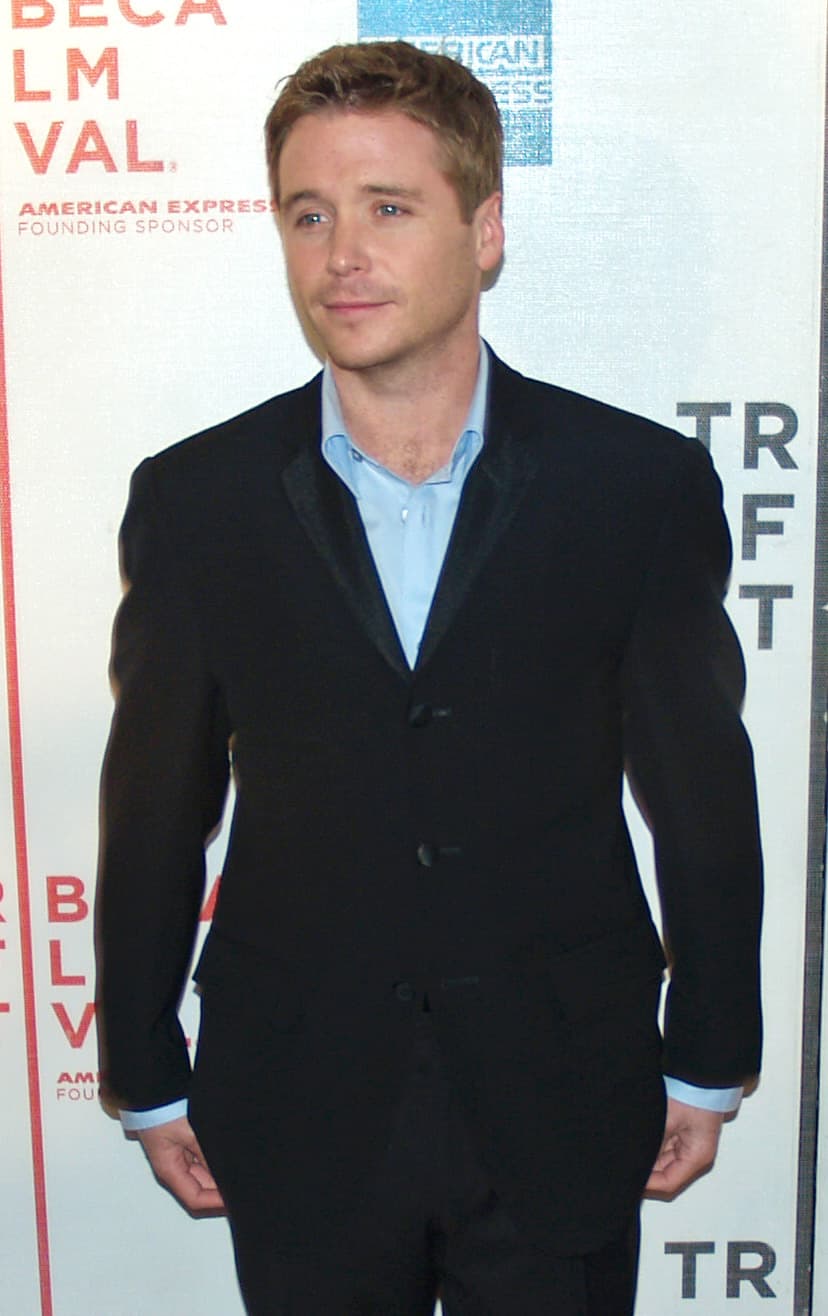 Kevin Connolly in a dark suit and blue shirt on a red carpet