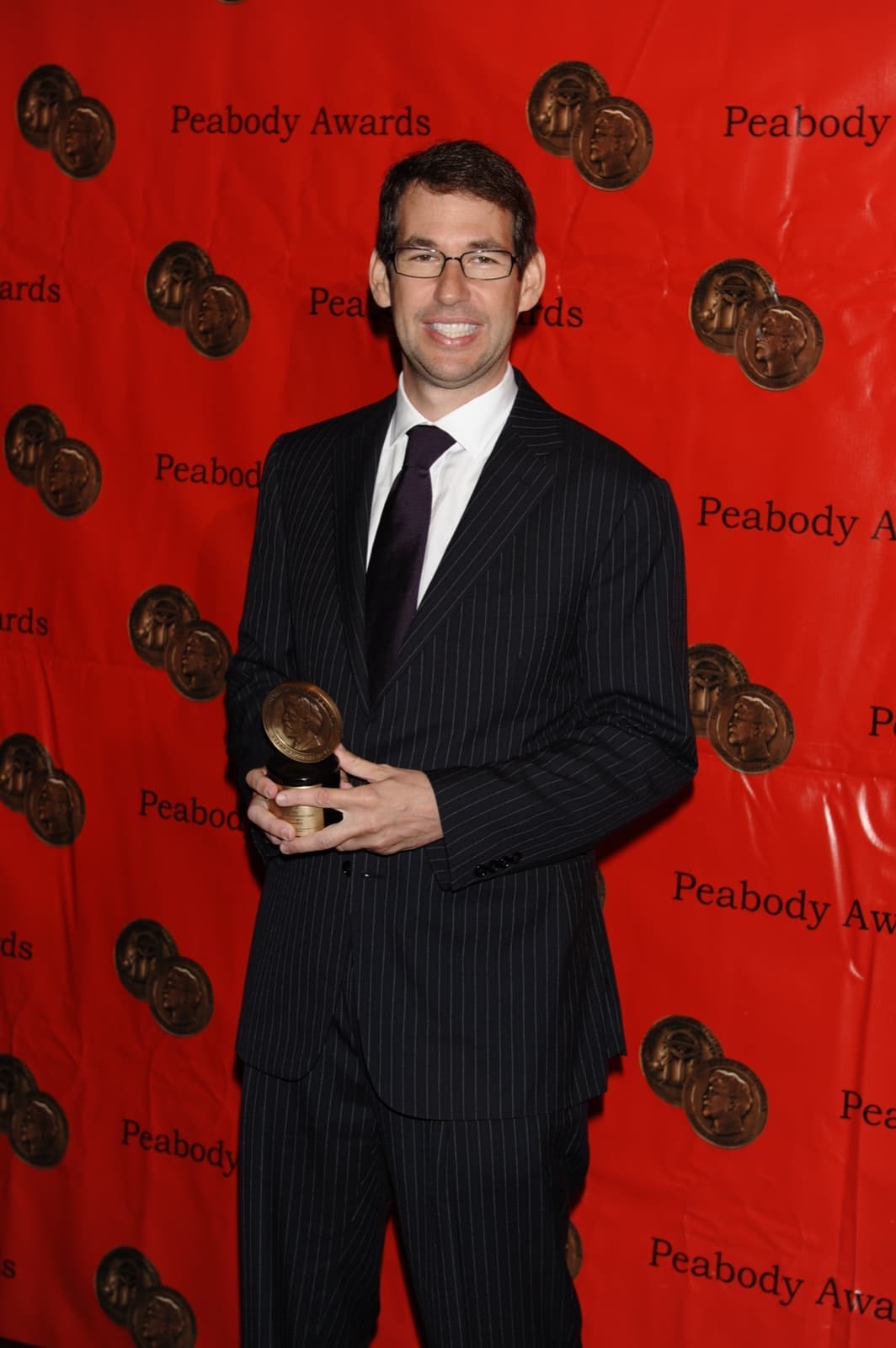Doug Ellin in a pinstripe suit holding a Peabody medal