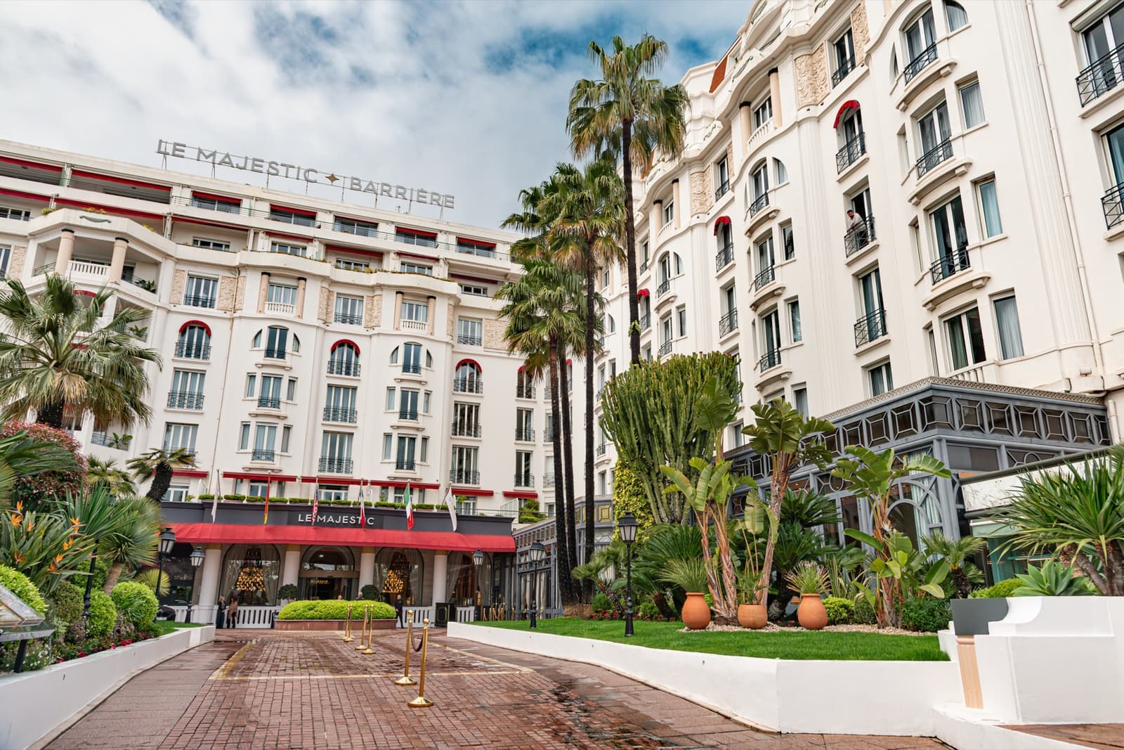 A white grand hotel behind palms and a red entrance canopy