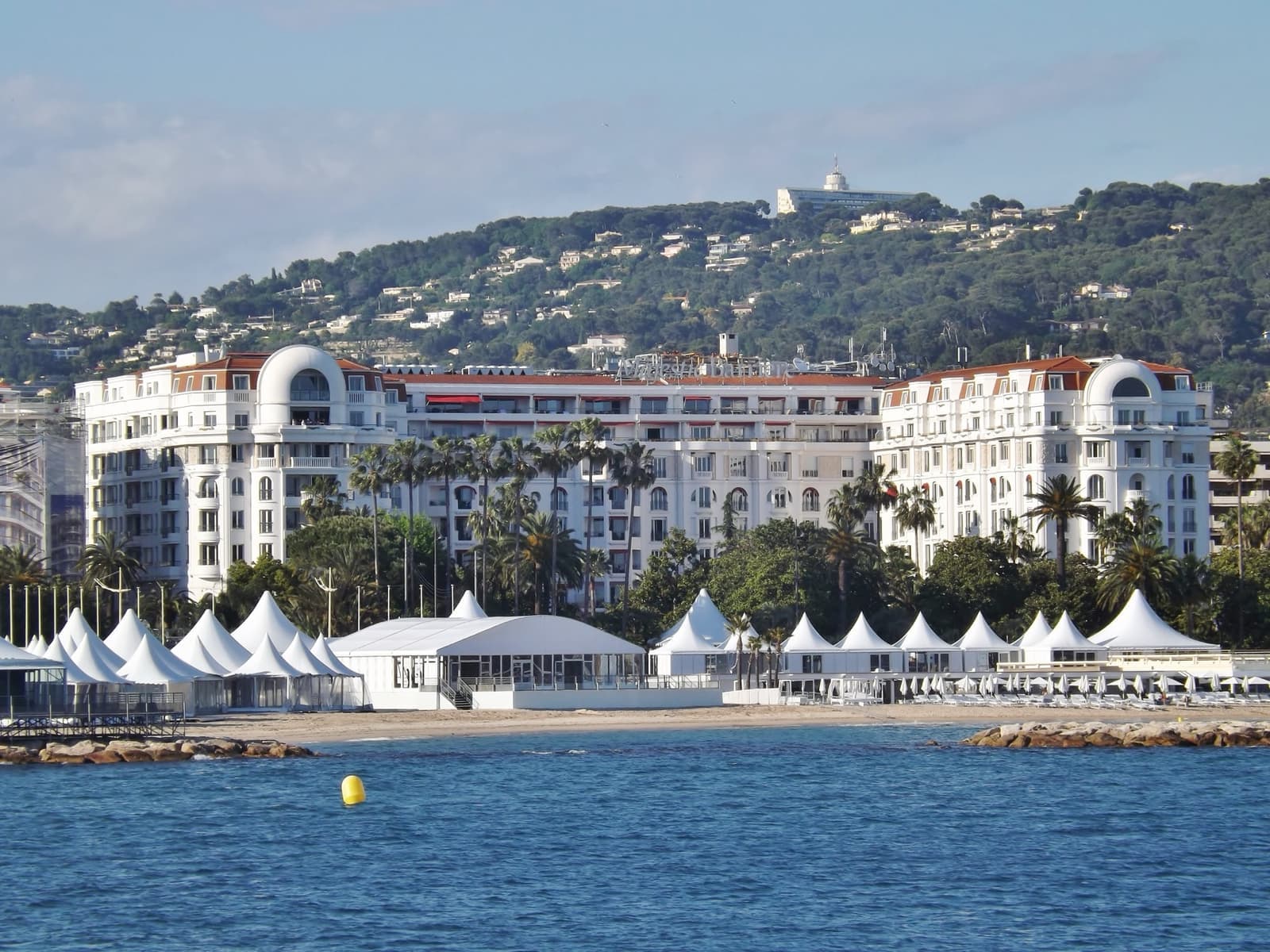 A white seafront hotel with white tents on the beach in front