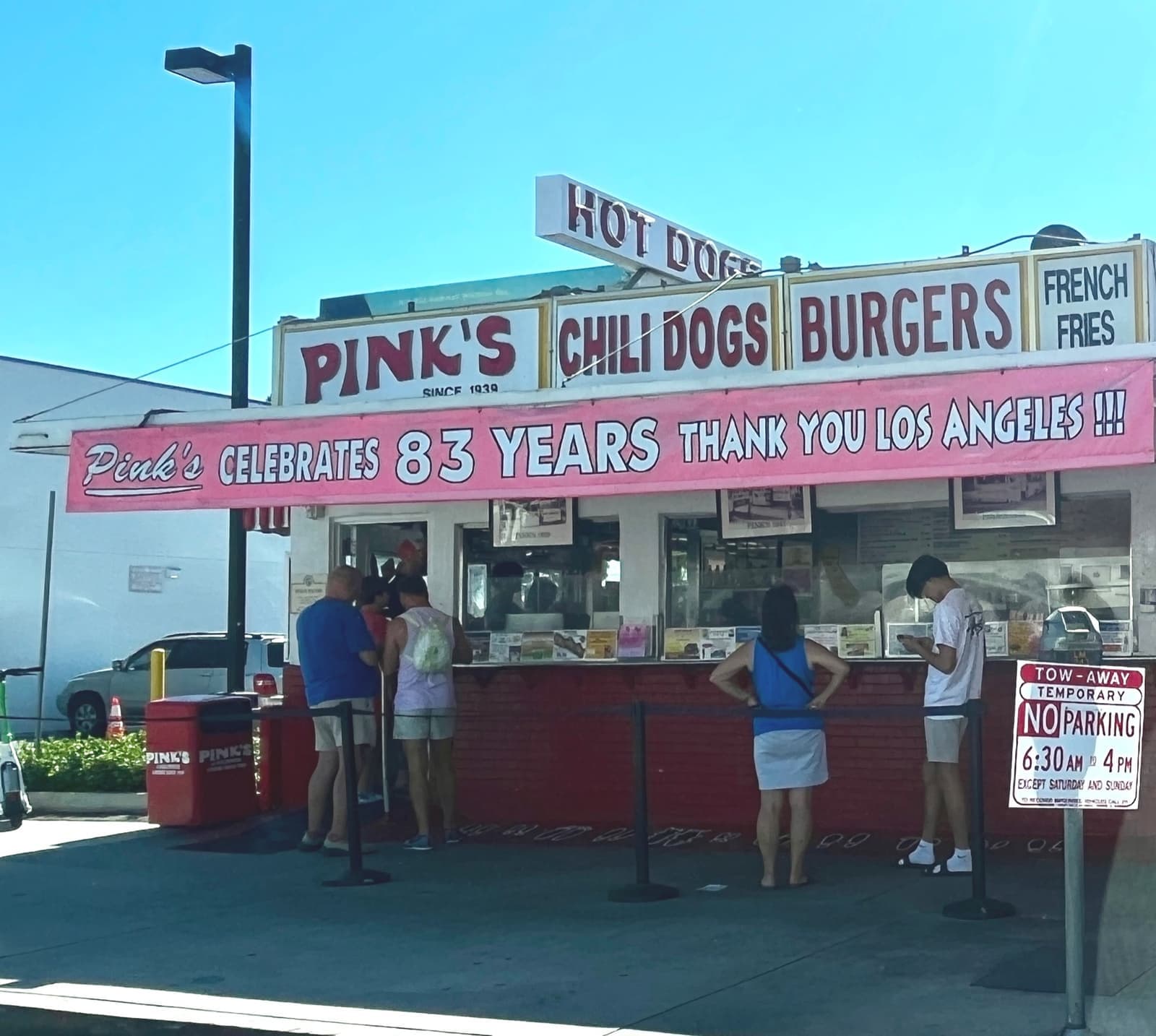 A pink-and-white hot dog stand with customers at the counter