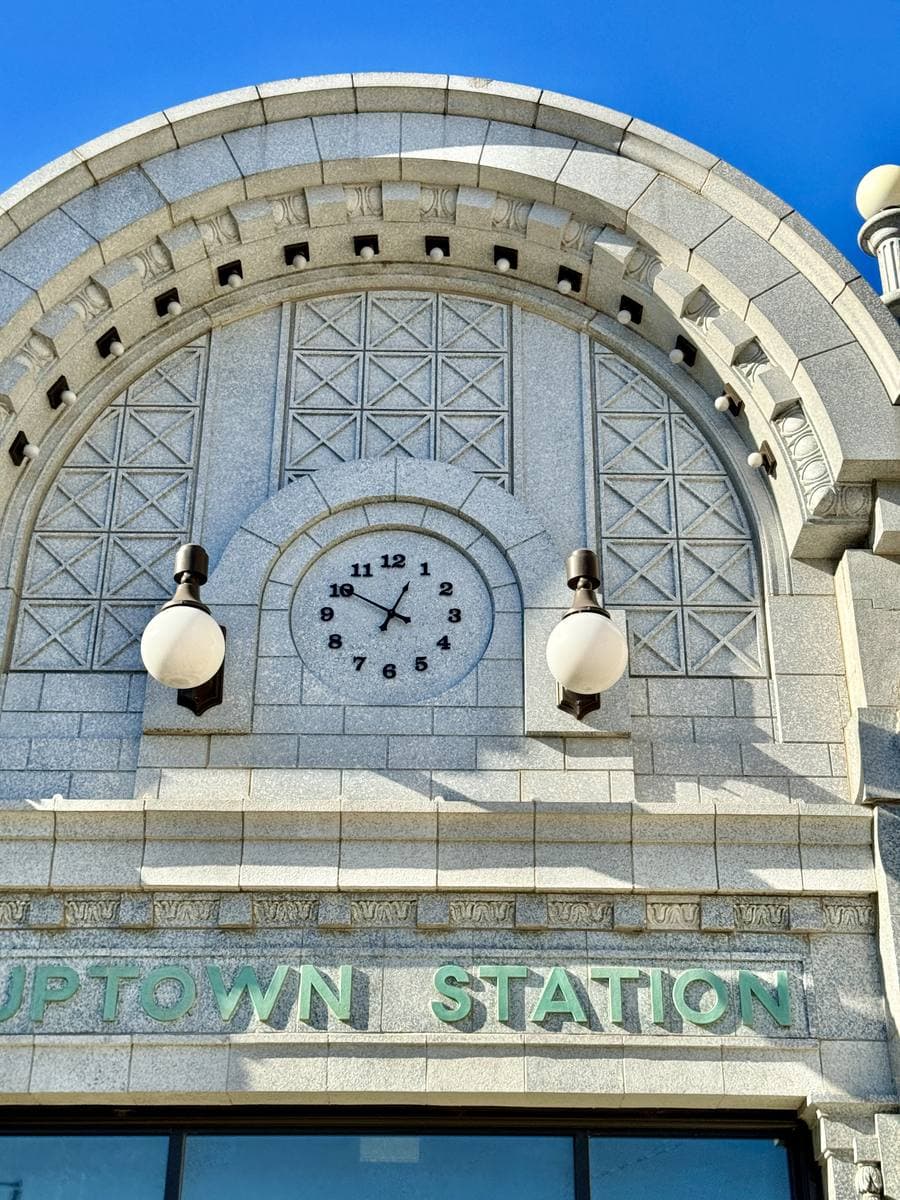 An ornate white terracotta arch with a clock, lettered Uptown Station