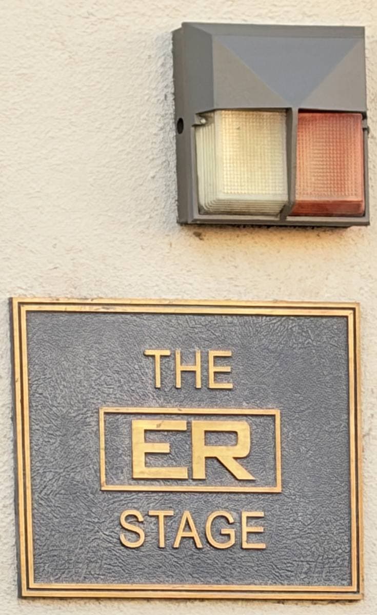 A bronze plaque reading The ER Stage beneath a two-colour stage light