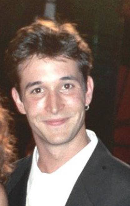 Noah Wyle in 1995, in a dark jacket and white shirt, smiling