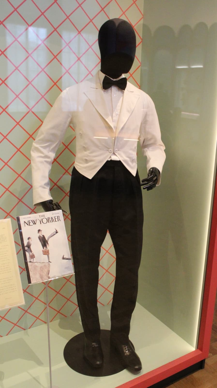 A white waiter’s jacket, black trousers and bow tie in a museum case